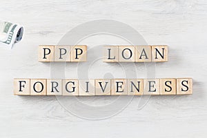 PPP LOAN Forgiveness text on wooden background with dollars roll