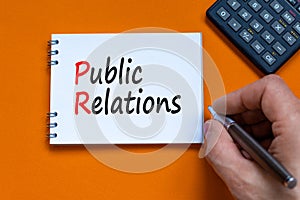 PR public relations symbol. Concept words PR public relations on white note. Businessman hand, calculator. Beautiful orange