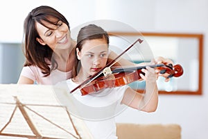 Practice makes perfect, my girl. A mother helping her daughter as she practices the violin - Copyspace.