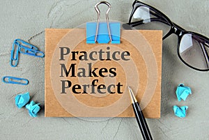 PRACTICE MAKES PERFECT - words on brown paper on the background of glasses, pens and paper clips