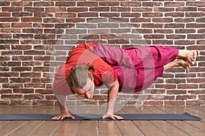 Practicing yoga idoor. Bearded longhair man doing Dwi Pada Koundinyasana pose