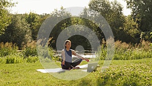 Practicing yoga and meditating in park with laptop. Woman sitting on yoga mat in park, watching online yoga exercises and meditati