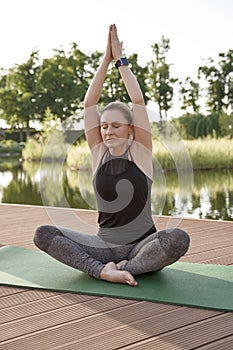 Practicing yoga in park. Full length of young beautiful woman in sportswear keeping eyes closed, sitting in lotus pose