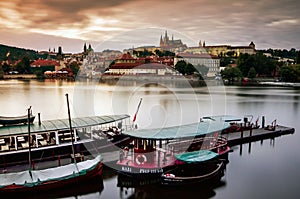 Prague castle view from the Vltava river bank, boats in front, during the dusk