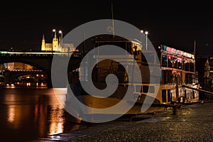 Prague at night, boat on the dock of the Vltava river, reflection of lights