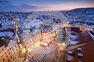 Prague Old Town in snow during late sunset with yellow lights and blue sky