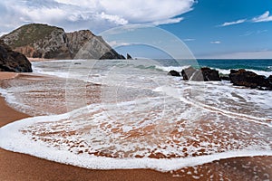 Praia da Adraga at atlantic ocean, Portugal. Foamy wave at sandy beach with picturesque landscape background