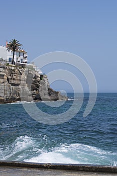 Praia da Azarujinha, beach in Estoril, portugal. waves and hill with house and palm