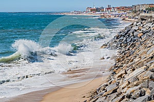 Selective focus of a wave on sand with a stone wall on Olinda beach with PÃÂ³voa de Varzim architecture breaking in blur in the bac