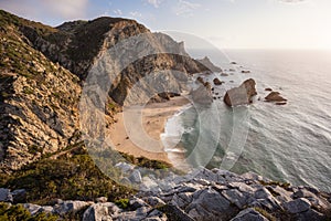 Praia da Ursa Beach at sunset, located in Sintra, Portugal. Landscape scene of sandy beach, sea stack rocks and ocean