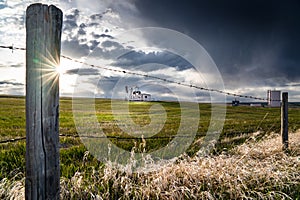 Prairie scene with barbed wire fence overlooking a distant oil pump jack under a stormy sky in Rocky View County Alberta