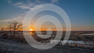 Prairie wetland / grassland and rural grassy dirt road landscape at sunset with orange, yellows, and blues in sky - Spring at the