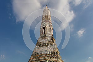 Prang of Wat Arun, Bangkok. Colorful exterior decorations statues cloudy blue sky.