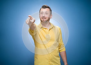 Prank man laughing at you and pointing with finger to the camera over blue background, dresses in yellow shirt. One guy with laugh