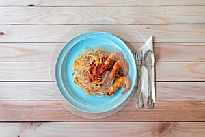 Prawn spaghetti pasta on blue plate, with fork & spoon on table