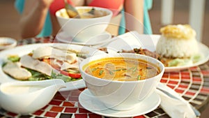 Prawn spicy soup is a Thai dish with sour and spicy taste. busty girl in a bikini eats Tom Yam at a table by the pool