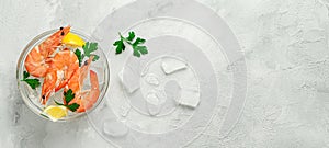 Prawns in a bowl with ice, lemon and parsley on grey background. Top view, copy space