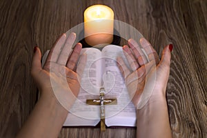 Pray. Female hands near the bible and candles on a wooden table