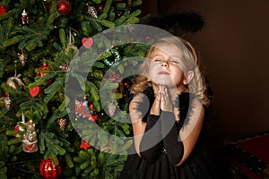 Pray a little girl in a black angel costume, looking with hope for peace. Happy childhood and peace. Christmas, New Year