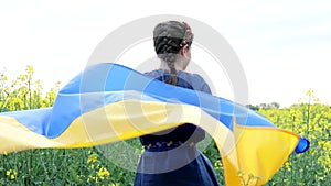 Pray for Ukraine. Child with Ukrainian flag in rapeseed field. Girl holding national flag in her hand.