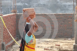 A rural female construction worker carrying heavy bricks with her hands over head.