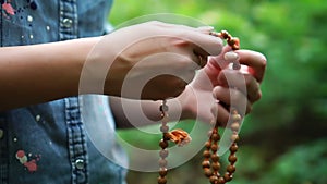 Prayer beads in hand. Female hand holding rosary, praying to god on green nature background, religious spirituality.
