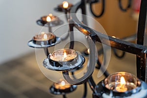 Prayer candles in black chandelier burning in church