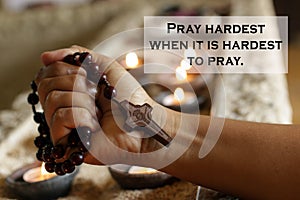 Prayer concept with Inspirational quote - Pray hardest when it is hardest to pray. With hand holding wooden rosary beads tightly.