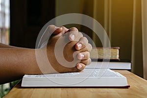 Prayer hands on a Holy Bible on wood table with window light.christian backgound.