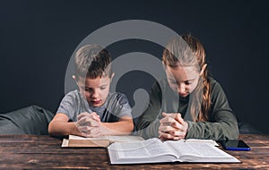 Prayer. An open Bible on the table. Two children pray with folded hands. Prayer in the family