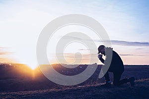 Prayer. Repentance. A man on his knees. Silhouette of a man on a blue sky background. Kneeling to God. Glorification.