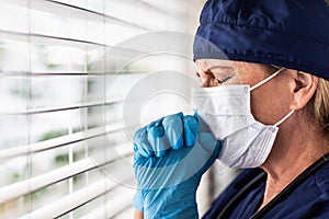 Prayerful Stressed Female Doctor or Nurse On Break At Window Wearing Medical Face Mask