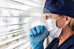 Prayerful Stressed Female Doctor or Nurse Crying At Window Wearing Medical Face Mask photo