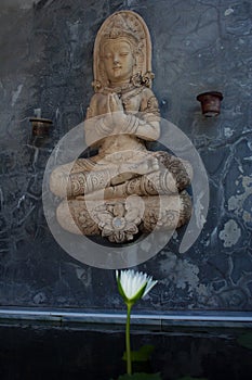 Praying buddha statue above opening white water lily flower