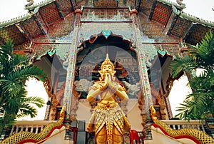 Praying Buddha statue standing at entrance of ancient Buddhist temple structure, Thailand