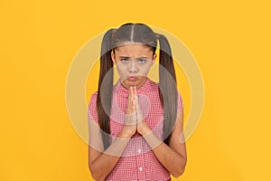 Praying girl child pray holding palms together in prayer gesture yellow background, plead