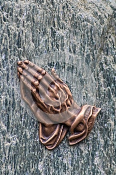 Praying hands as bronze figure on a graveyard grave as religious symbol for faith christianity blessing catholic priest and belief