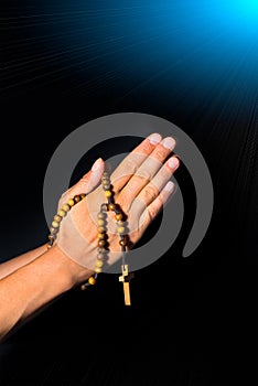 Praying Hands holding rosary beads on black background