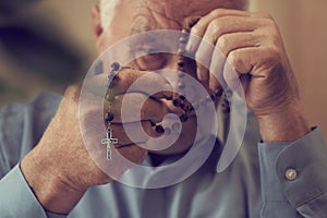 Praying hands of an old man holding rosary beads.