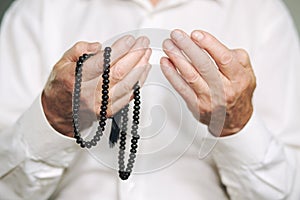 Praying hands of an old man holding rosary beads