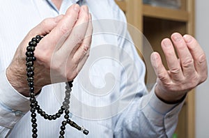 Praying hands of an old man holding rosary beads