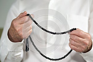 Praying hands of an old man with rosary beads