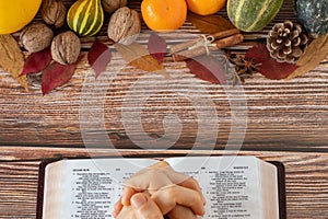 Praying hands-on open Holy Bible with colorful fall fruits food on wooden table. A thanksgiving concept.