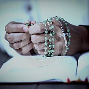 Praying hands of woman with rosary and bible