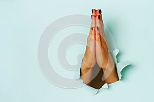 Praying hands of young woman through torn blue paper background. Christianity, church, worship concept. Banner with copy space