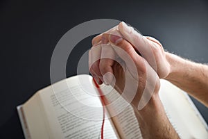 Praying with interlocked fingers and religious book on black background