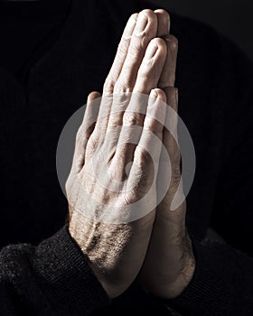 Praying male hands infront of a dark background