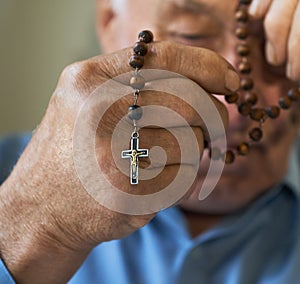 Praying old man with hands holding rosary beads.