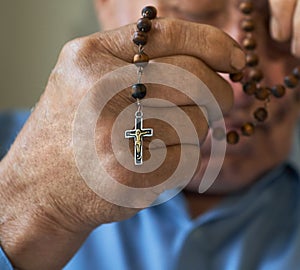 Praying old man with hands holding rosary beads.