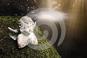 Praying stone angel on moss in front of waterfall